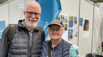 Grauhaariger Mann mit Brille und grauhaarige Frau mit Brille vor Volksbund-Stand