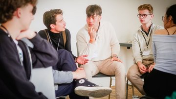 Fünf junge Menschen sitzen im Halbkreis und reden miteinander.