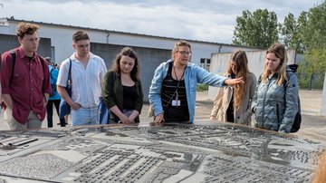 Sechs Menschen stehen an einem Relief, das das frühere KZ abbildet