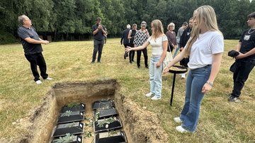 Eine Grube mit mehreren Särgen: Zwei Mädchen stehen davor und werfen Blumen hinein.