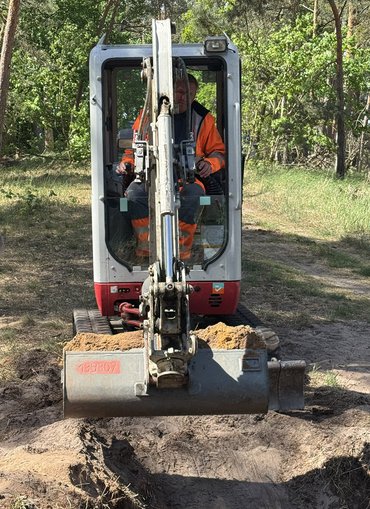 Kleiner Bagger im Wald mit Schaufel voller Sand