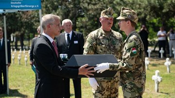 Ein Mann im Anzug übergibt einem Soldaten einen Pappsarg.