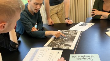 Vier junge Menschen sitzenan einem Tisch und beugen sich über ein historisches Foto.