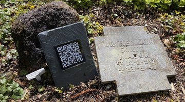 Liegendes Grabkreuz aus Stein mit QR-Code, daneben aufgestellt