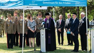 Soldaten, Zivilisten und Geistliche stehen unter einem Volksbund-Pavillon 