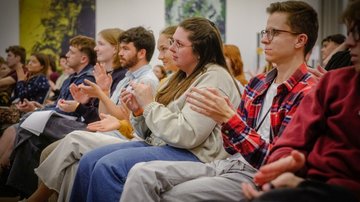 Junge Menschen sitzen auf Stühlen und applaudieren.