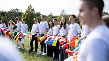 Eine Gruppe junger Menschen steht mit einheitlichen Volksbund-T-Shirts in einer Reihe und hält ein Band mit zahlreichen Flaggen.