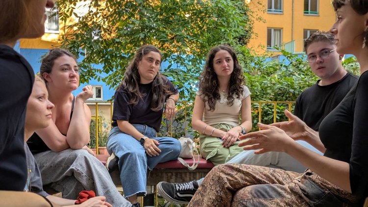 Eine Gruppe junger Menschen sitzt in einem Hinterhof im Halbkreis