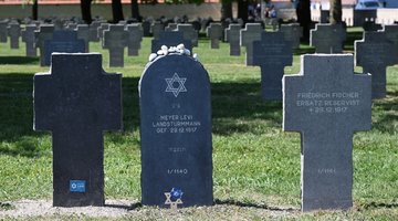 Eine Grabstele zwischen Grabkreuzen auf einem Friedhof
