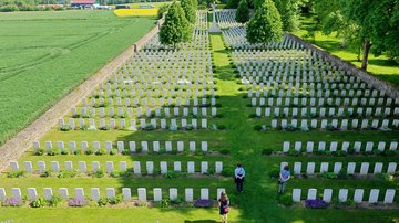 Soldatenfriedhof aus der Luft mit weißen Grabsteinen und drei Besucherinnen im Vordergrund
