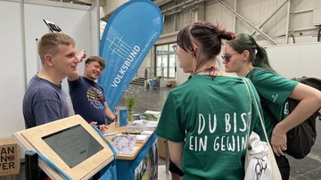 Zwei junge Frauen mit grünen T-Shirts stehen vor dem Volksbund-Stand.