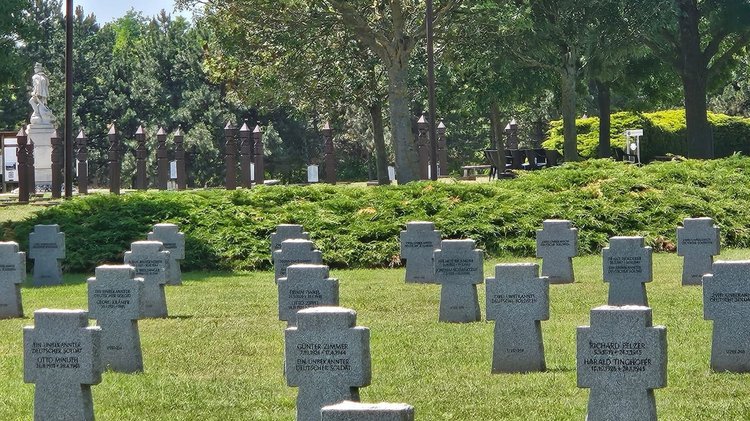 Grabkreuze auf einer Rasenfläche, im Hintergrund die Volksbund- und die deutsche Fahne