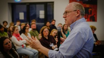 Mann mit Mikrofon steht vor sitzendem Publikum